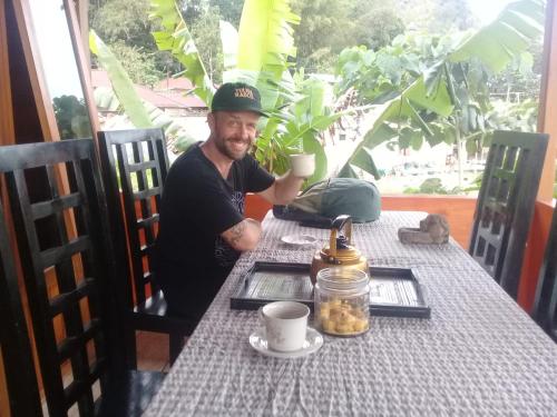 a man sitting at a table with a cup of coffee at THE SINGKI HOME FAMILY in Rantepao