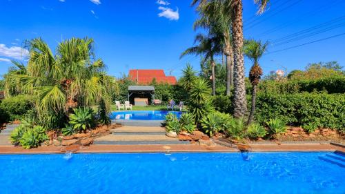 a swimming pool with palm trees and a house at Country Leisure Motor Inn in Dubbo