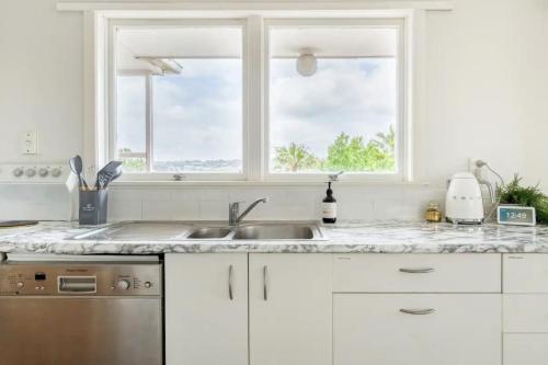 a white kitchen with a sink and two windows at Bright & Central Home in Auckland