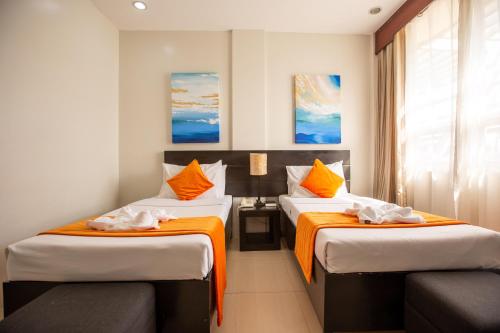 una camera d'albergo con due letti con lenzuola arancioni di Holiday Suites a Città di Puerto Princesa