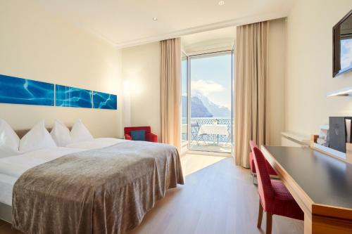 ein Hotelzimmer mit einem Bett, einem Schreibtisch und einem Fenster in der Unterkunft Seehotel Waldstätterhof Swiss Quality in Brunnen