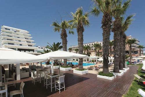 a resort with a pool and palm trees and tables and umbrellas at Vrissiana Boutique Beach Hotel in Protaras