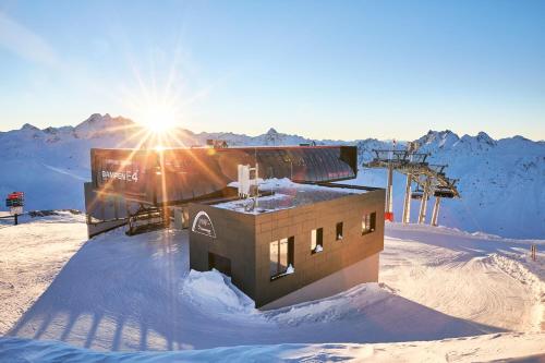 a building in the snow with the sun behind it at Hotel Rosanna by Alpeffect Hotels in Sankt Anton am Arlberg