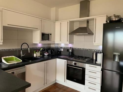 a kitchen with white cabinets and a black refrigerator at Sea View Penthouse Marina Apartment in Portishead