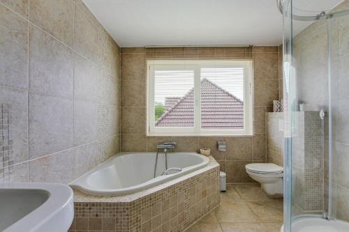 a bathroom with a tub and a toilet and a window at Big Family villa 12p big garden with bathtub and jacuzzi in Zeewolde