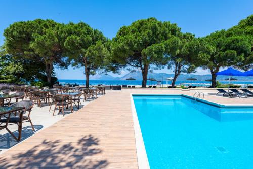 a swimming pool with tables and chairs and trees at Porto Rio Hotel in Patra