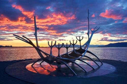 a statue of a boat on the water with a sunset at Lundur Apartments - Down Town in Reykjavík