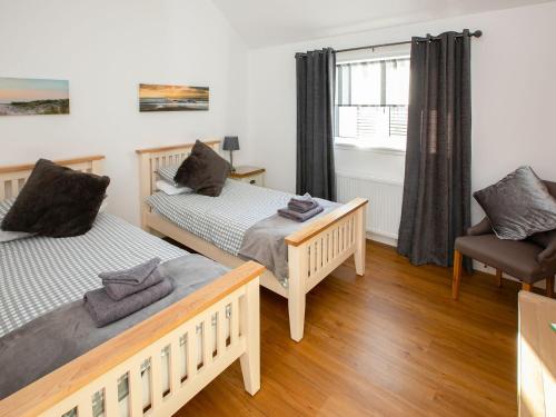 a bedroom with two beds and a chair at Rossie Cottage in Auchterarder