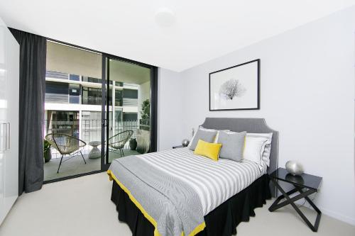 a white bedroom with a bed and a balcony at CityStyle Apartments - BELCONNEN in Canberra