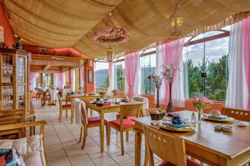 ein Esszimmer mit Tischen, Stühlen und Fenstern in der Unterkunft Carícia do Vento Pousada Boutique in Monte Verde