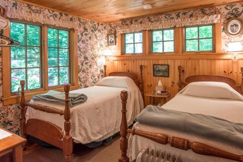 two beds in a room with wooden walls and windows at FRE-Wil in Lincolnville
