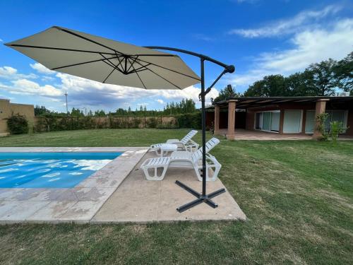 einen Tisch und einen Stuhl mit einem Sonnenschirm neben einem Pool in der Unterkunft Pergolas Guest House - Pileta, Vinos y Montaña in Vista Flores