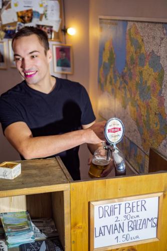 a man standing behind a table with a bottle of beer at Cinnamon Sally Backpackers Hostel in Rīga