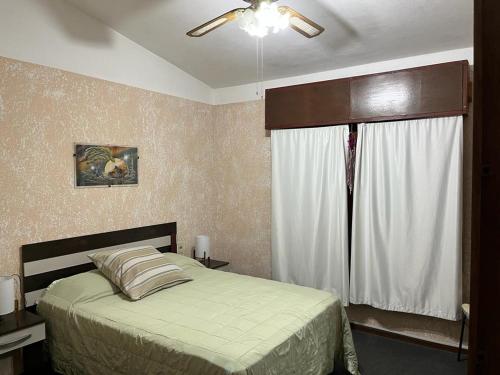 1 dormitorio con 1 cama, ventilador de techo y ventana en Barrio Country, en Piriápolis