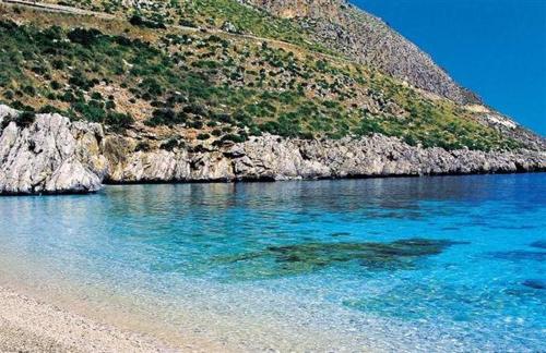 a beach with blue water next to a mountain at Casale la Macina Residence Scopello in Scopello