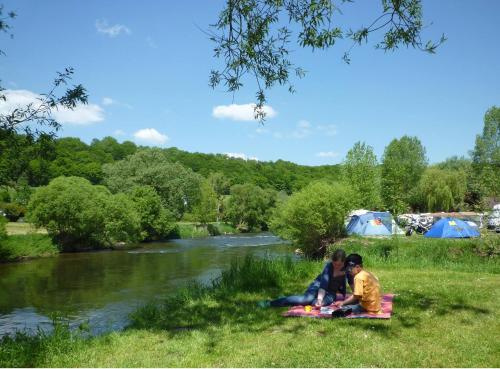 two people sitting on a blanket next to a river at Leaf camping Reisdorf in Reisdorf