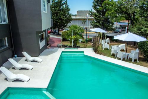 une piscine avec des chaises blanches et un bâtiment dans l'établissement Hotel Terrazas by CPH, à Villa Carlos Paz