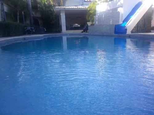 a pool of blue water with a slide and a dog at Hotel Cambri in Nagua