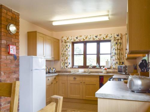 een keuken met houten kasten en een witte koelkast bij Stildon Manor Cottage in Pensax