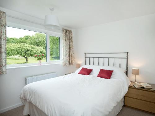 a bedroom with a white bed with red pillows and a window at Little Orchard in Farmborough