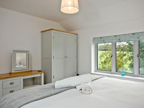 a bedroom with a white bed with a dresser and windows at Oakwood in Saint Endellion