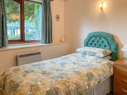 a bedroom with a bed with a blue headboard and a window at Forge Mill Cottage in Dalbeattie