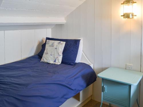 a bed with a blue pillow and a blue table at Beach Corner Cottage in Gorran Haven