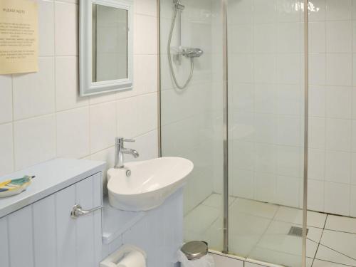 a bathroom with a sink and a glass shower at Beach Corner Cottage in Gorran Haven