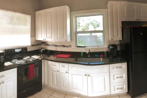 a kitchen with white cabinets and a black refrigerator at Historic 1920 Bungalow Minutes from DTSP in St Petersburg
