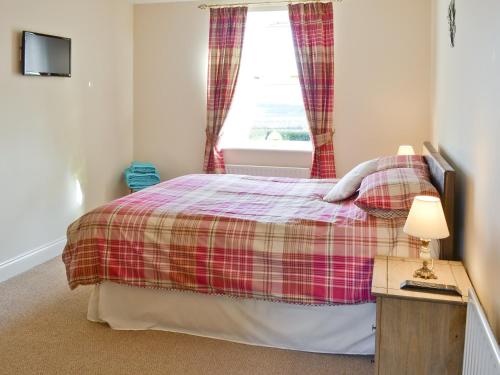 a bedroom with a bed with a plaid blanket and a window at Heckley Cottage in Alnwick