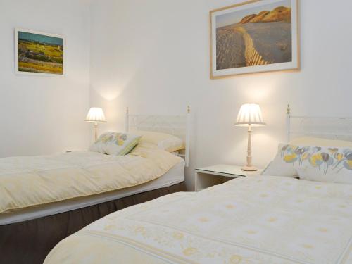 two beds in a white room with two lamps at West Lawn in Rhosneigr