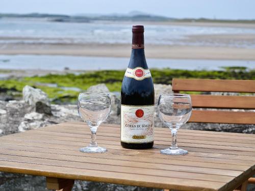 a bottle of wine and two wine glasses on a wooden table at West Lawn in Rhosneigr