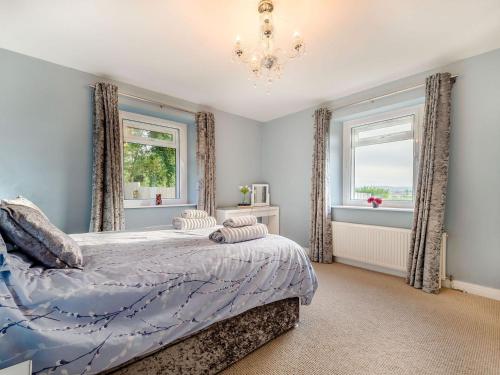a bedroom with a bed and two windows and a chandelier at Shawdon Hill Cottage in Glanton