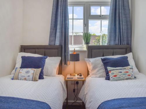 two beds in a bedroom with blue curtains and a window at Seashell House in Burnham on Sea