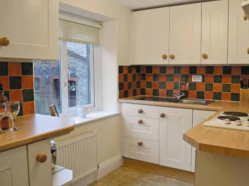 a kitchen with white cabinets and a sink and a window at Penhill Farm Cottage in Fremington