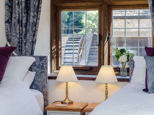 two beds in a room with a window and two lamps at Stable Cottage in Uley