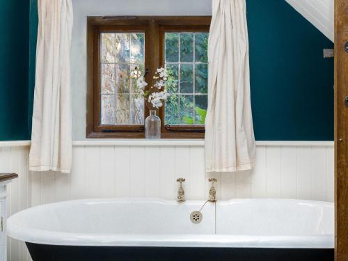 baño con bañera blanca y ventana en Stable Cottage en Uley