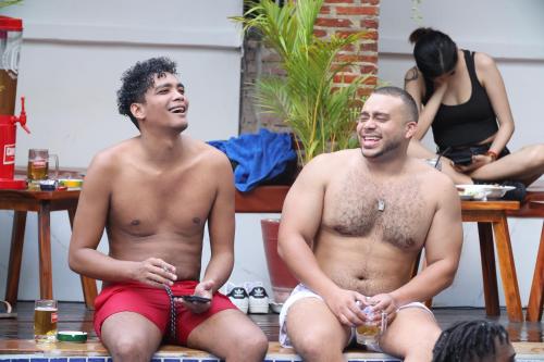 two shirtless men sitting on a bench with drinks at Bliss & Beats Hostel in Phnom Penh