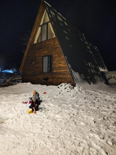 a child sitting in the snow in front of a cabin at Landhaus Borjomi in Borjomi