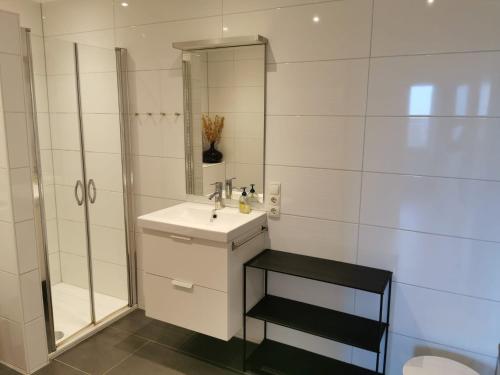 uma casa de banho branca com um lavatório e um chuveiro em FeWo Nordsee-Perle Meerblick - Horumersiel em Horumersiel