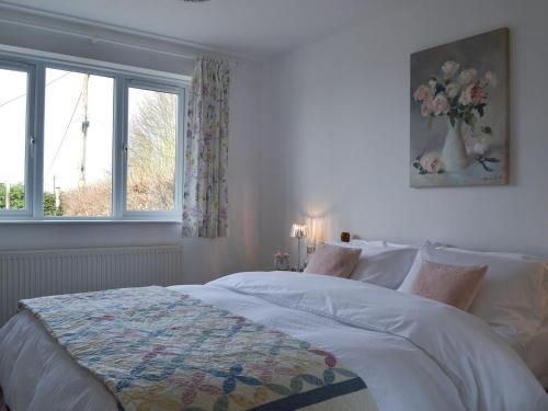 een witte slaapkamer met een bed met een vaas met bloemen bij Miners Cottage in Clowne