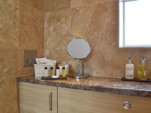 a bathroom counter with a mirror and bottles on it at Miners Cottage in Clowne