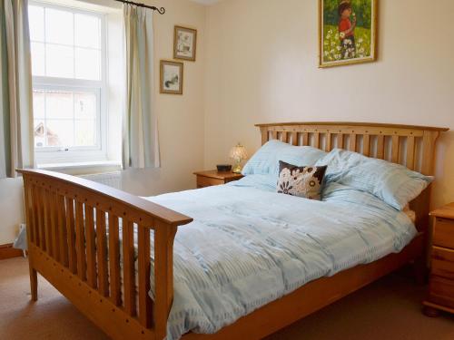 a bedroom with a wooden bed and a window at Hollyhocks Cottage in Docking
