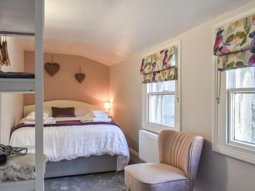 a bedroom with a bed and a chair and two windows at The Cottage Highfield in Rothbury