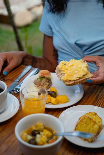 a table with plates of food and a person holding a sandwich at Pousada Cacau in Praia do Rosa
