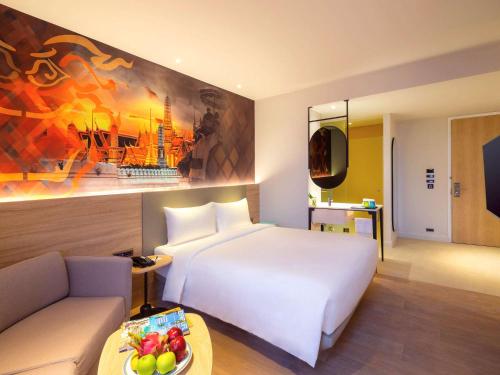 ibis Styles Bangkok Ratchada في بانكوك: غرفة الفندق بسرير ابيض واريكة
