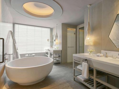 a white bathroom with a tub and a sink at Mövenpick Siam Hotel Na Jomtien Pattaya in Na Jomtien