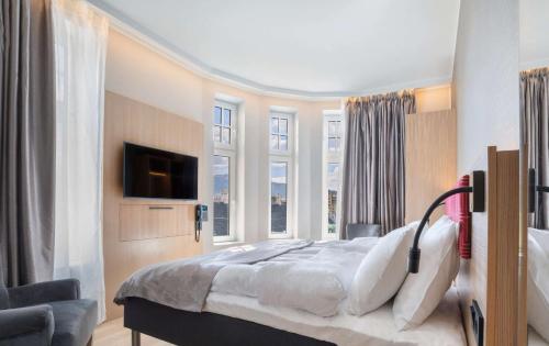 a bedroom with a bed and a tv and windows at Bergen Harbour Hotel, WorldHotels Crafted in Bergen