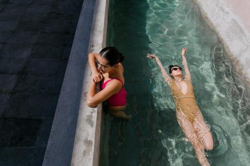 two women are in a swimming pool at Casa Oxa Hotel in Querétaro