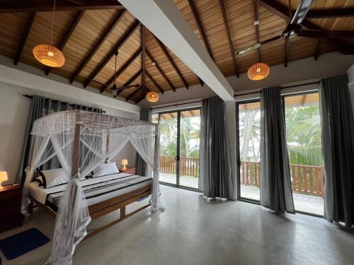 a bedroom with a canopy bed and large windows at Galawatta Beach Resort in Unawatuna